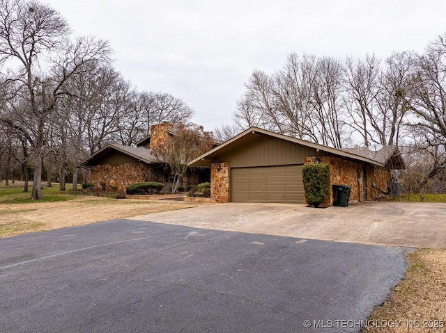 view of front facade with stone siding, central AC, driveway, and an attached garage