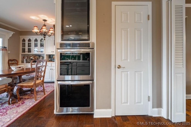 kitchen with glass insert cabinets, an inviting chandelier, dark wood finished floors, white cabinetry, and stainless steel double oven