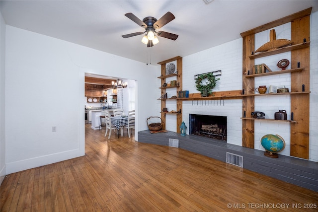 living room with ceiling fan with notable chandelier, a fireplace, and hardwood / wood-style floors