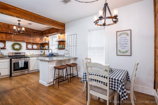 kitchen featuring stainless steel gas stove, a notable chandelier, decorative light fixtures, and white cabinets