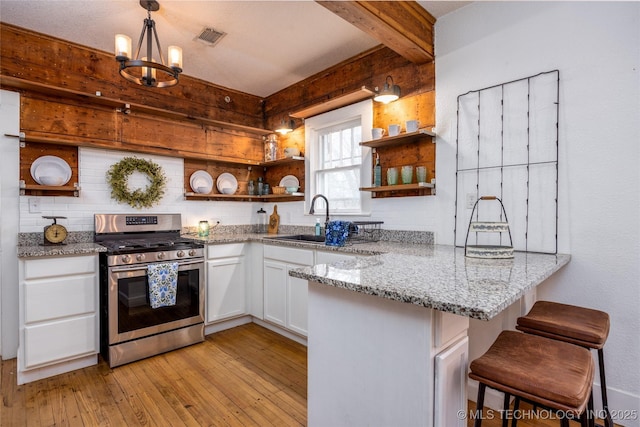 kitchen featuring a breakfast bar, gas range, white cabinetry, decorative light fixtures, and kitchen peninsula