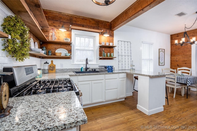 kitchen featuring decorative light fixtures, sink, white cabinets, light stone counters, and gas range