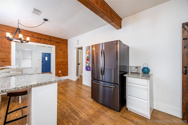 kitchen with pendant lighting, stainless steel refrigerator, wood walls, light stone counters, and light wood-type flooring