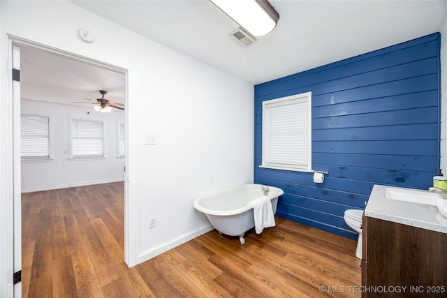 bathroom with ceiling fan, vanity, wood-type flooring, a tub, and toilet