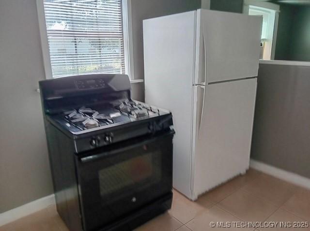 kitchen with light tile patterned flooring, black range with gas stovetop, and white fridge