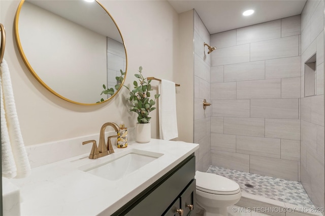 bathroom with a tile shower, toilet, recessed lighting, and vanity