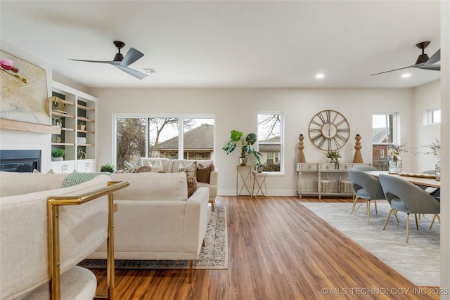 living area featuring a glass covered fireplace, ceiling fan, wood finished floors, and recessed lighting