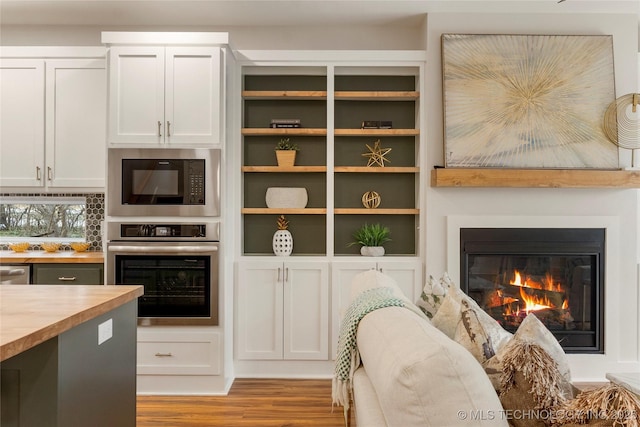 interior space with wood finished floors, butcher block countertops, a glass covered fireplace, black microwave, and stainless steel oven