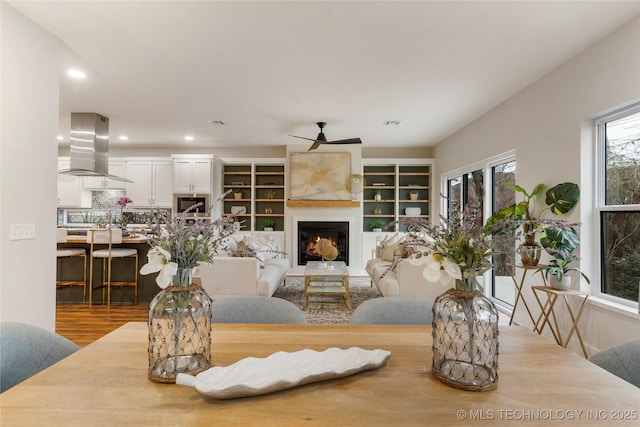 living area with recessed lighting, wood finished floors, a ceiling fan, and a warm lit fireplace