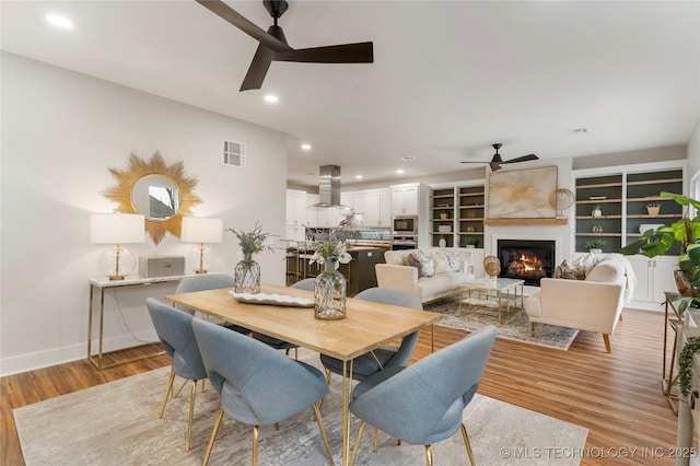 dining area with recessed lighting, ceiling fan, light wood finished floors, a glass covered fireplace, and visible vents
