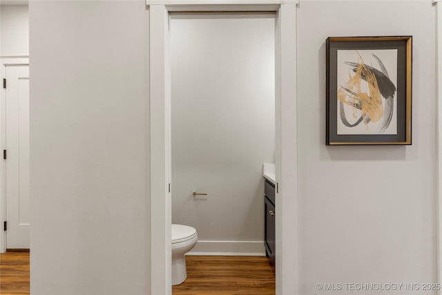 bathroom featuring baseboards, wood finished floors, toilet, and vanity