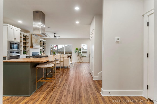 kitchen with appliances with stainless steel finishes, wooden counters, baseboards, open floor plan, and island exhaust hood