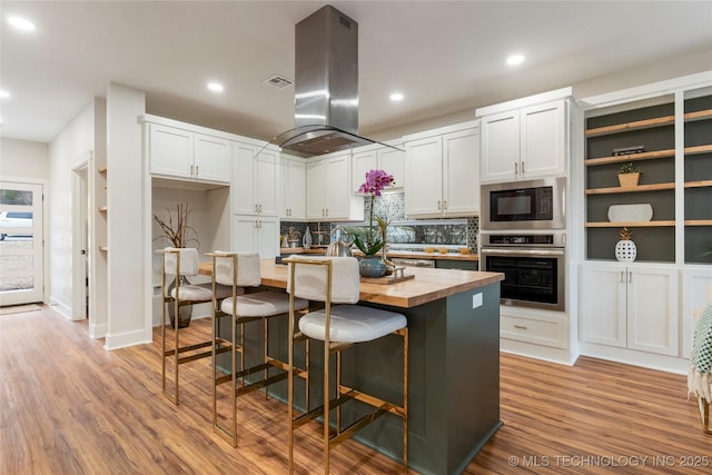 kitchen with wooden counters, light wood finished floors, island exhaust hood, black microwave, and stainless steel oven
