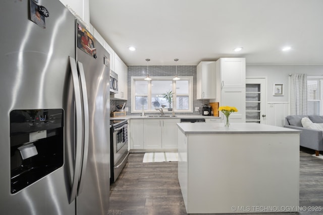 kitchen with decorative light fixtures, a kitchen island, white cabinets, and appliances with stainless steel finishes