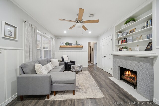 living room featuring ornamental molding, dark hardwood / wood-style flooring, built in features, ceiling fan, and a fireplace