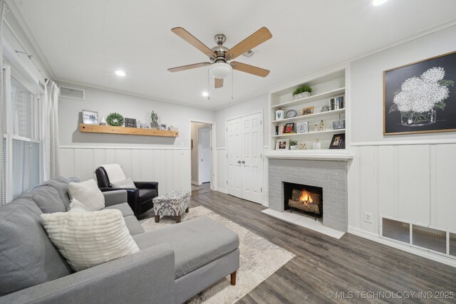 living room featuring built in features, ceiling fan, a fireplace, ornamental molding, and dark hardwood / wood-style flooring