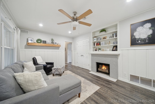 living room with crown molding, ceiling fan, dark hardwood / wood-style floors, a brick fireplace, and built in shelves