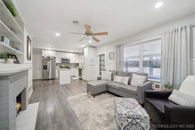 living room with ceiling fan, ornamental molding, a fireplace, and light wood-type flooring