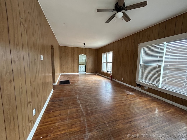 unfurnished living room featuring dark hardwood / wood-style floors, ceiling fan, and wood walls