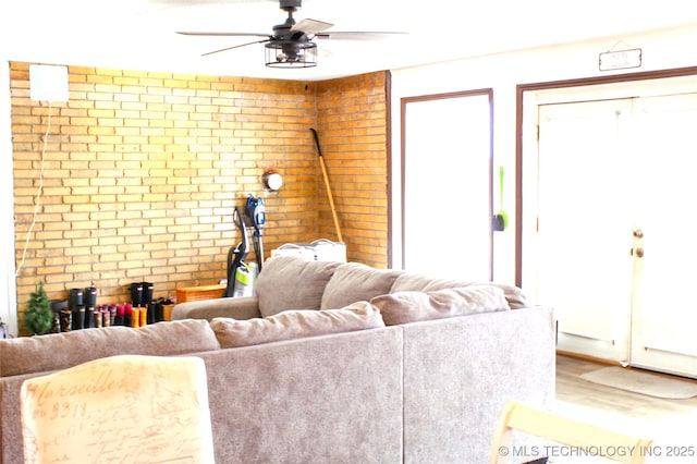 living room featuring wood-type flooring, brick wall, plenty of natural light, and ceiling fan