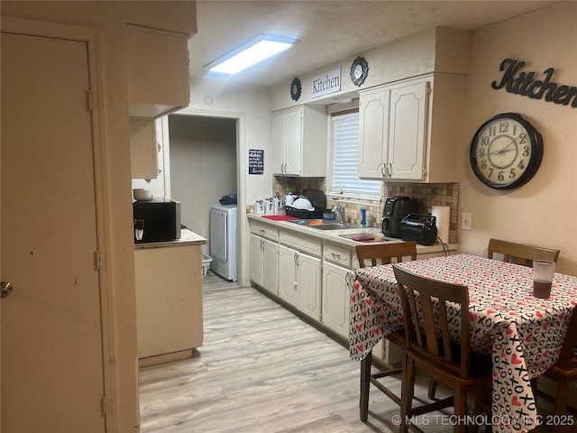 kitchen with washer / dryer, sink, white cabinetry, light hardwood / wood-style floors, and backsplash