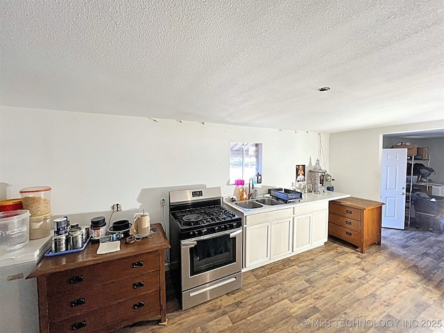 kitchen with sink, stainless steel gas range, light hardwood / wood-style floors, and a textured ceiling