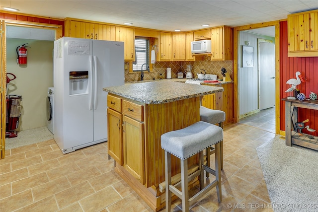 kitchen with washer and dryer, a breakfast bar area, decorative backsplash, a center island, and white appliances