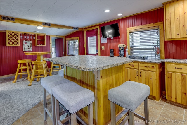 kitchen with light colored carpet, a breakfast bar, and wood walls