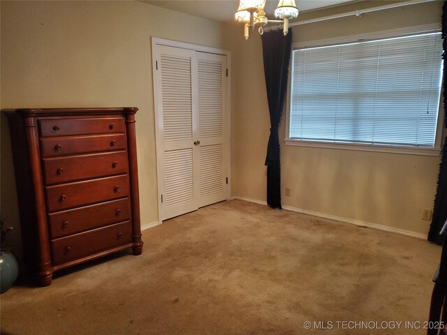 unfurnished bedroom featuring light carpet, an inviting chandelier, and a closet