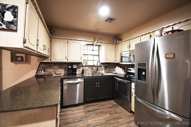 kitchen featuring stainless steel appliances, a sink, dark countertops, dark wood-type flooring, and tasteful backsplash