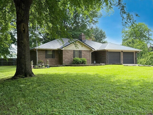 ranch-style home featuring a chimney, an attached garage, brick siding, metal roof, and a standing seam roof