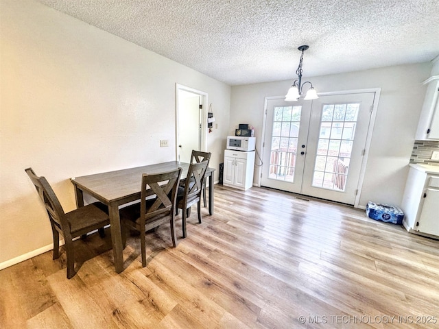 dining area featuring french doors, a textured ceiling, a chandelier, and light hardwood / wood-style flooring