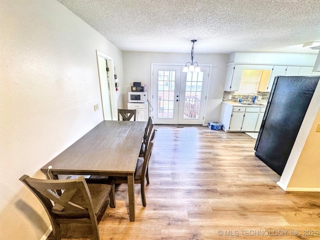 dining room with french doors, sink, light hardwood / wood-style flooring, and a textured ceiling