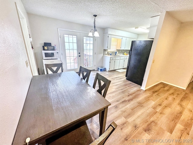 dining room with a textured ceiling, light wood-type flooring, and french doors