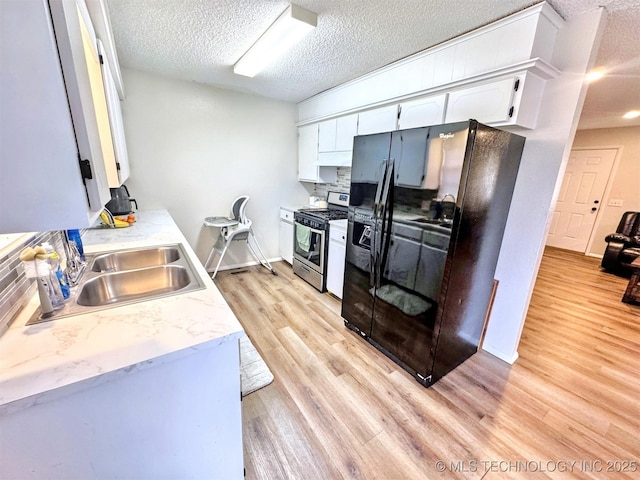 kitchen featuring white cabinetry, sink, black fridge, stainless steel range with gas stovetop, and light hardwood / wood-style flooring