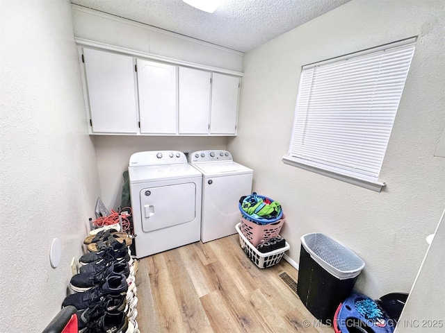 laundry area with cabinets, light wood-type flooring, a textured ceiling, and washer and clothes dryer