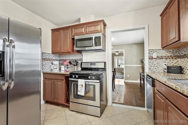 kitchen featuring backsplash, light tile patterned flooring, ceiling fan, stainless steel appliances, and light stone countertops