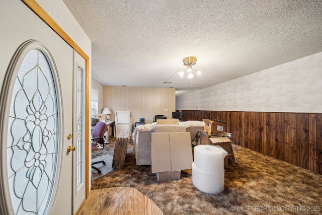 living room with dark colored carpet, a textured ceiling, and wood walls