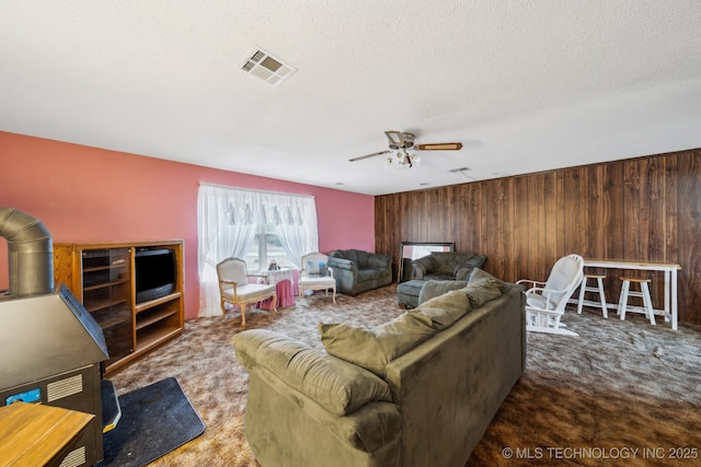 carpeted living room featuring ceiling fan, wooden walls, and a textured ceiling