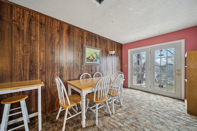 carpeted dining area with a textured ceiling and wood walls