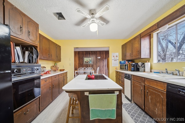 kitchen featuring sink, a breakfast bar, black appliances, a textured ceiling, and a kitchen island