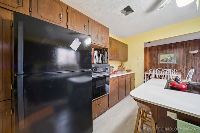 kitchen with a breakfast bar area, black appliances, light hardwood / wood-style floors, a textured ceiling, and wood walls