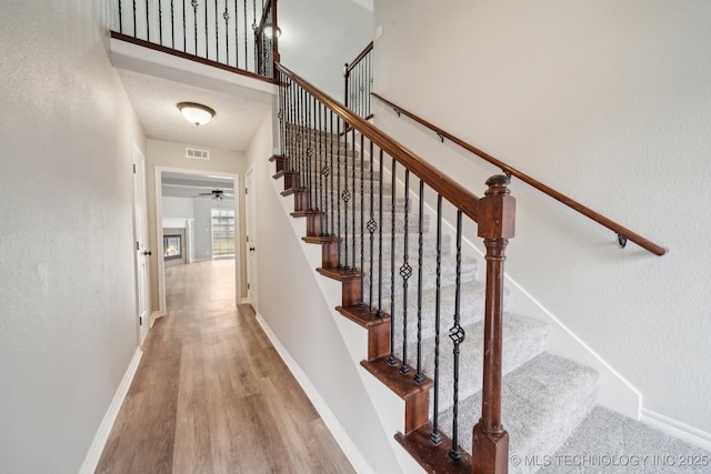 stairs with hardwood / wood-style floors, a textured ceiling, ceiling fan, and a high ceiling