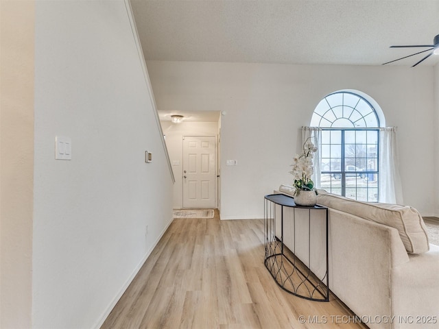 interior space featuring a textured ceiling, baseboards, a ceiling fan, and light wood-style floors