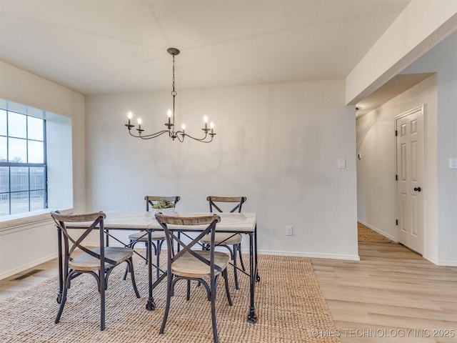 dining space featuring baseboards, light wood finished floors, visible vents, and a notable chandelier