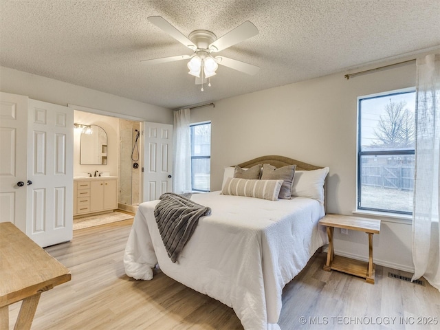 bedroom with a textured ceiling, connected bathroom, a ceiling fan, baseboards, and light wood-type flooring