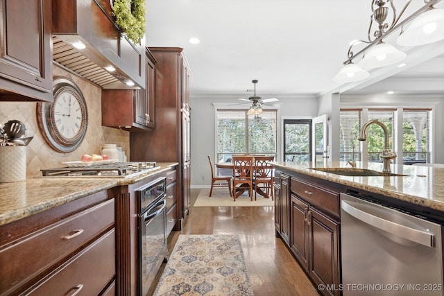 kitchen with sink, appliances with stainless steel finishes, pendant lighting, light stone countertops, and wall chimney range hood