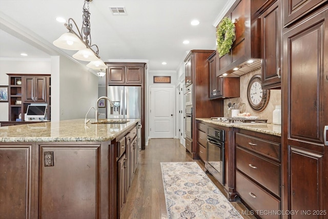 kitchen with wall chimney exhaust hood, sink, decorative light fixtures, ornamental molding, and an island with sink