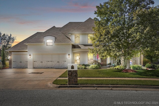 french provincial home featuring a front yard, a garage, driveway, and a shingled roof