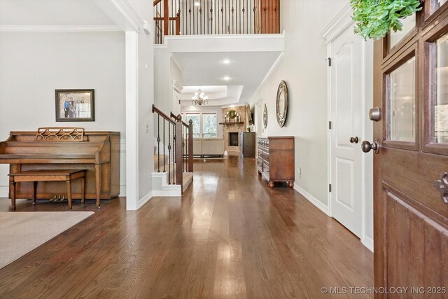 foyer featuring wood finished floors, an inviting chandelier, crown molding, baseboards, and stairs